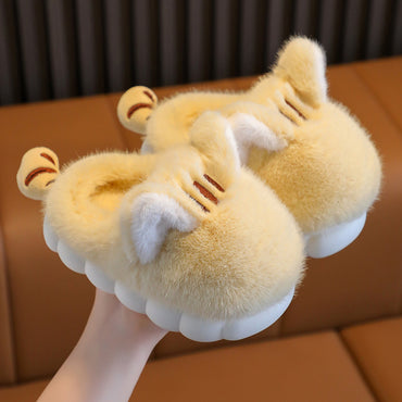 Pair of fluffy yellow slippers with cat ears on a brown surface.